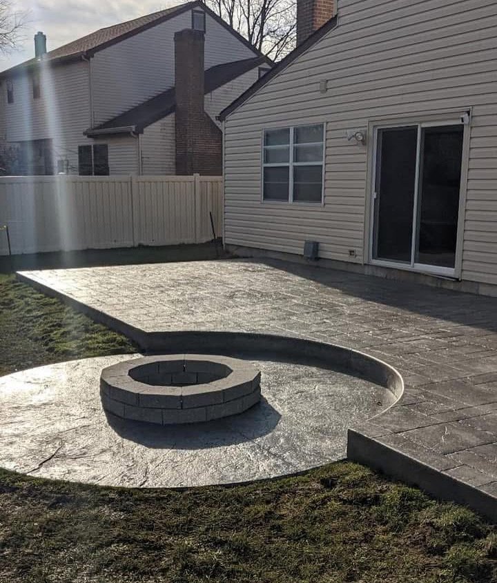 Decorative concrete patio with circular fire pit installation in a residential backyard, showcasing craftsmanship by U.S. Concrete Construction in South Jersey.