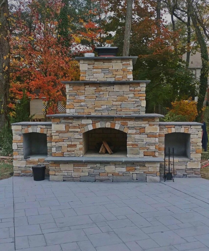 Outdoor stone fireplace with stacked stone design, surrounded by autumn foliage, showcasing craftsmanship by U.S. Concrete Construction for home enhancement in South Jersey.